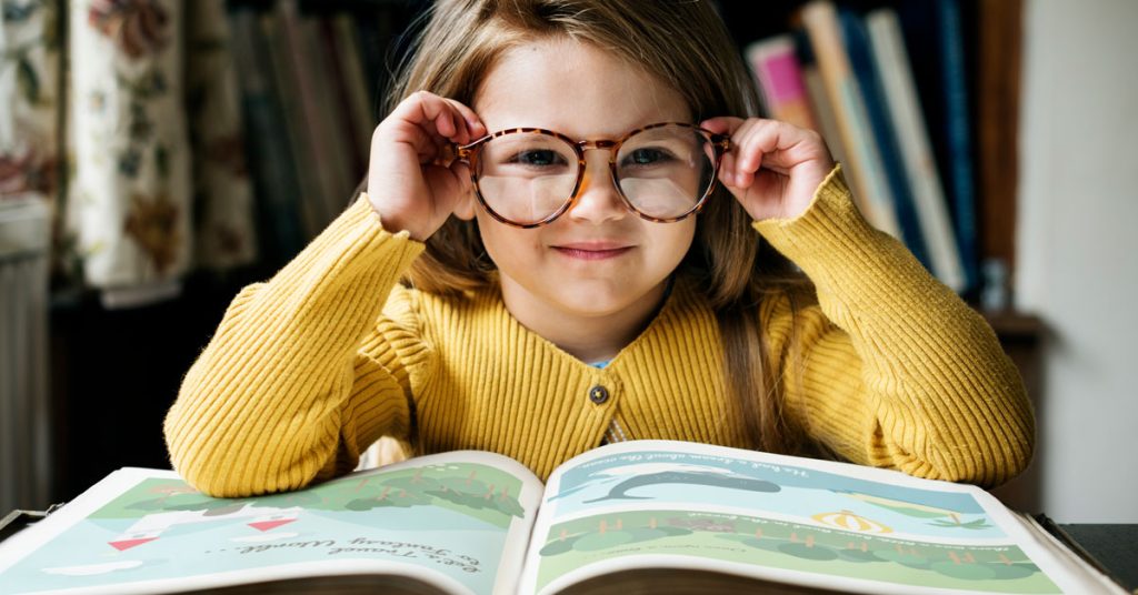 Niña sonriendo mientras lee un libro en inglés