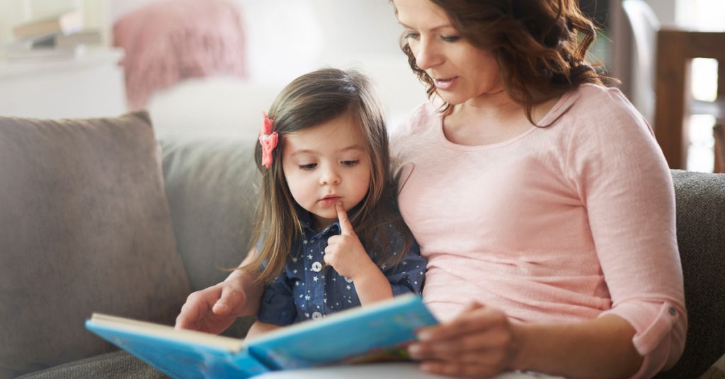 Niña leyendo un libro en inglés junto a su mamá