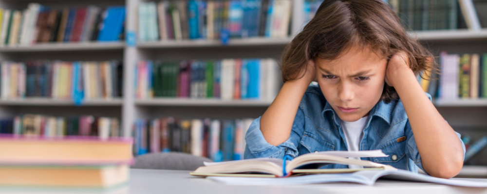 Niño sentado frente a un libro de inglés, demostrando lo difíciles que son los métodos tradicionales para aprender ese idioma.